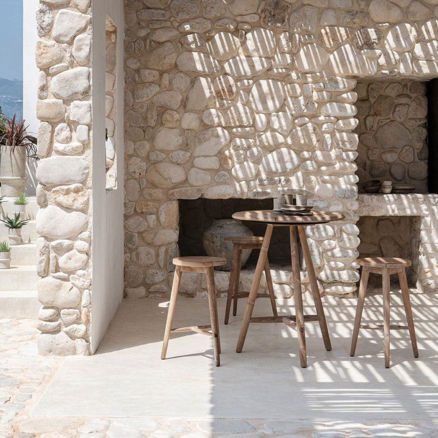 Runder Outdoor Bartisch Faye aus massivem Teakholz mit 75 cm Durchmesser und 95 cm Höhe im Ambiente mit Barhocker | Gommaire bei STUFF Shop kaufen