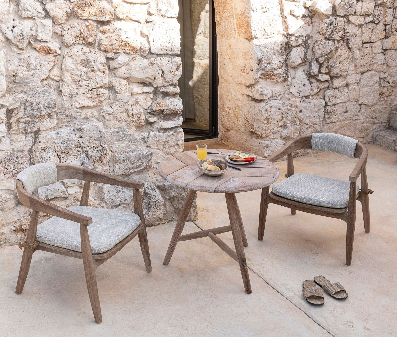 Niedriger runder Outdoor Bistrotisch Faye aus Teakholz im Ambiente mit dem Sessel Faye | Gommaire bei STUFF Shop kaufen