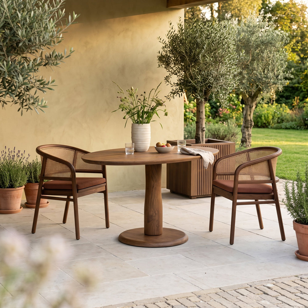 Bistrotisch Dita Oval Teak Emas Brown von Gommaire, Teak Emas Brown, 120 × 86 × H 76 cm, mit Armlehnenstühlen Imen, Pflanzkübel Nora und Vase Simon auf der Gartenterrasse