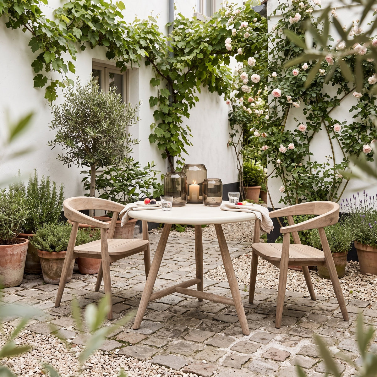 Bistrotisch Faye rund Beton Teak Natural Grey von Gommaire, Beton und Teak Natural Grey, Ø 75 × H 76 cm, Interiorbild mit Armlehnstühlen Faye und Windlicht Daniel im Innenhof