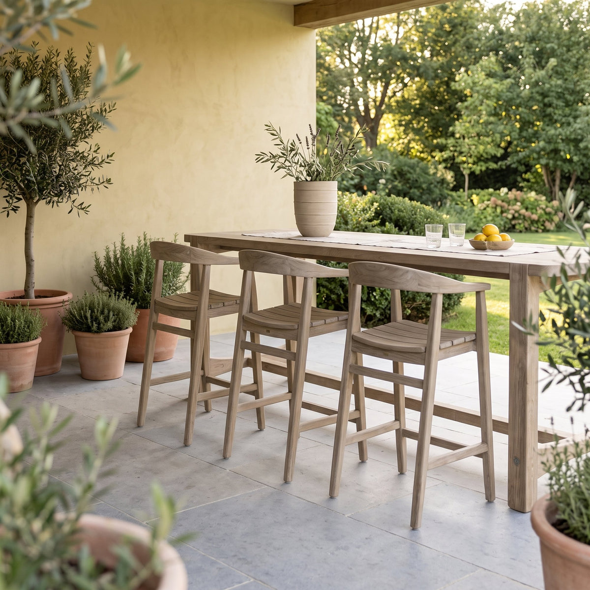 Barstuhl Faye Teak Natural Grey von Gommaire, Teak Natural Grey, B 54 × T 51 × H 94 cm, am Bartisch Jacoba mit Vase Simon auf der Gartenterrasse