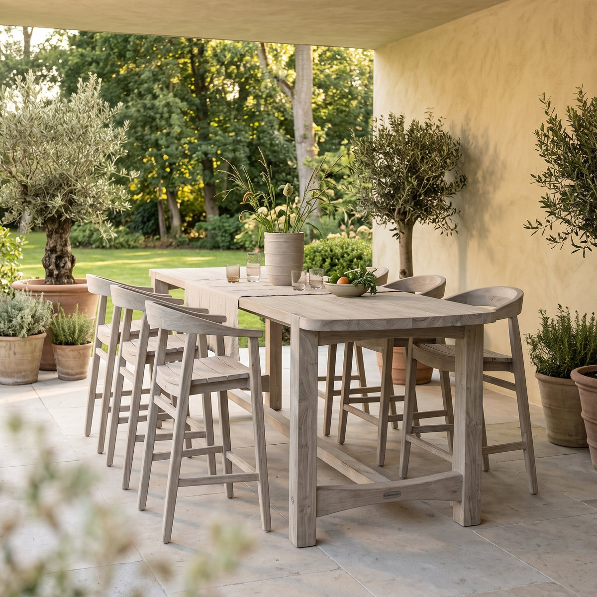 Bartisch Jacoba Teak Natural Grey von Gommaire, Teak Natural Grey, 300 × 97 × H 95 cm, mit Barstühlen Faye und Vase Simon auf der Gartenterrasse