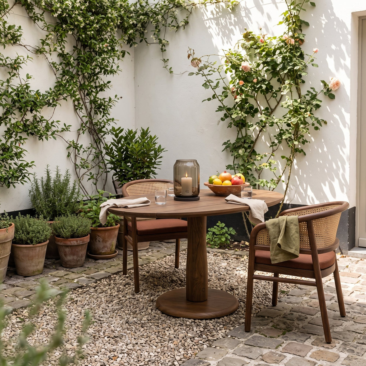 Bistrotisch Dita Oval Teak Emas Brown von Gommaire, Teak Emas Brown, 120 × 86 × H 76 cm, mit Armlehnenstühlen Imen und Windlicht Daniel im Innenhof