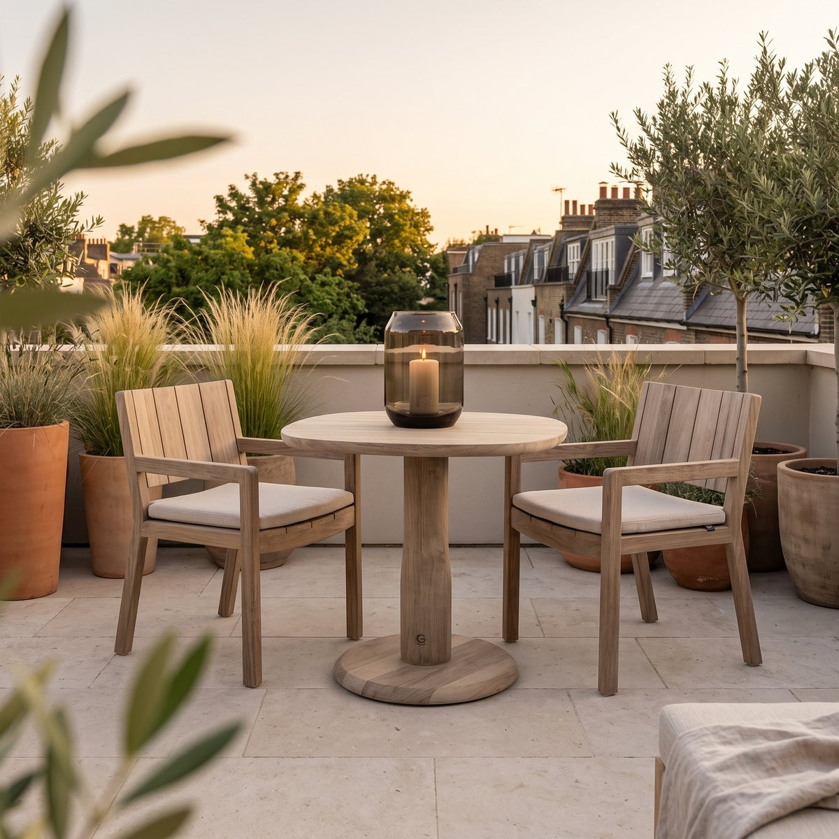 Bistrotisch Dita Squircle Teak Natural Grey von Gommaire, Teak Natural Grey, Ø 80 × H 76 cm, mit Armlehnstühlen Mario und Windlicht Daniel auf der Dachterrasse
