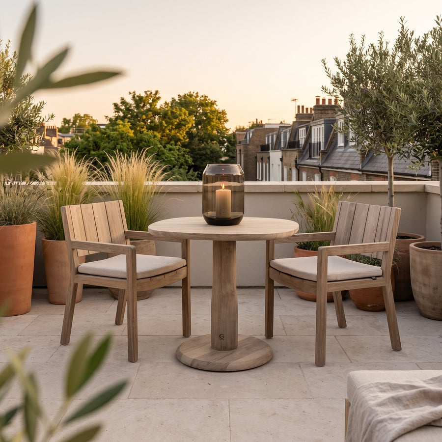 Bistrotisch Dita Squircle Teak Natural Grey von Gommaire, Teak Natural Grey, Ø 80 × H 76 cm, mit Armlehnstühlen Mario und Windlicht Daniel auf der Dachterrasse