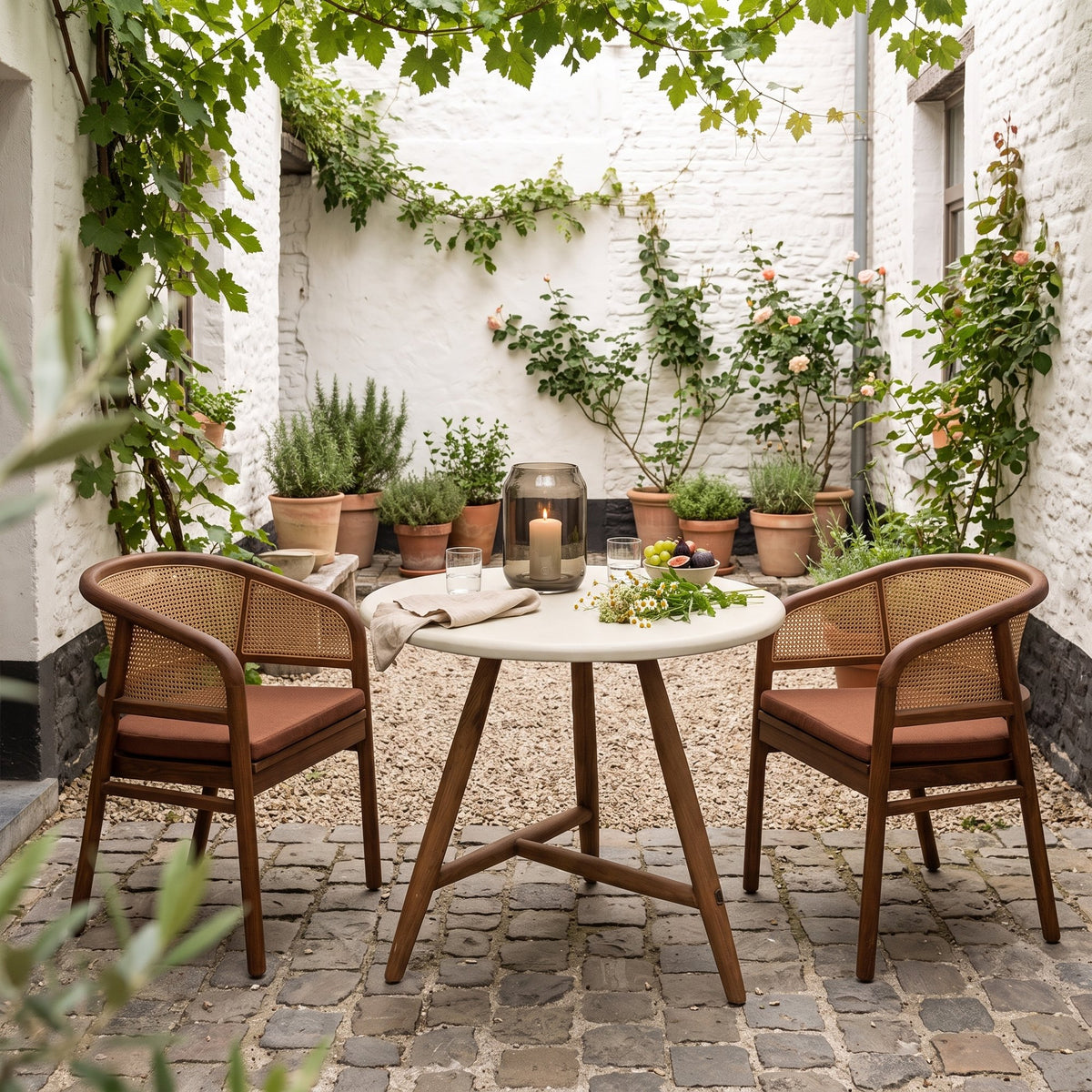 Bistrotisch Faye rund Beton Teak Emas Brown von Gommaire, Beton und Teak Emas Brown, Ø 75 × H 76 cm, Interiorbild mit Armlehnenstühlen Imen und Windlicht Daniel im Innenhof