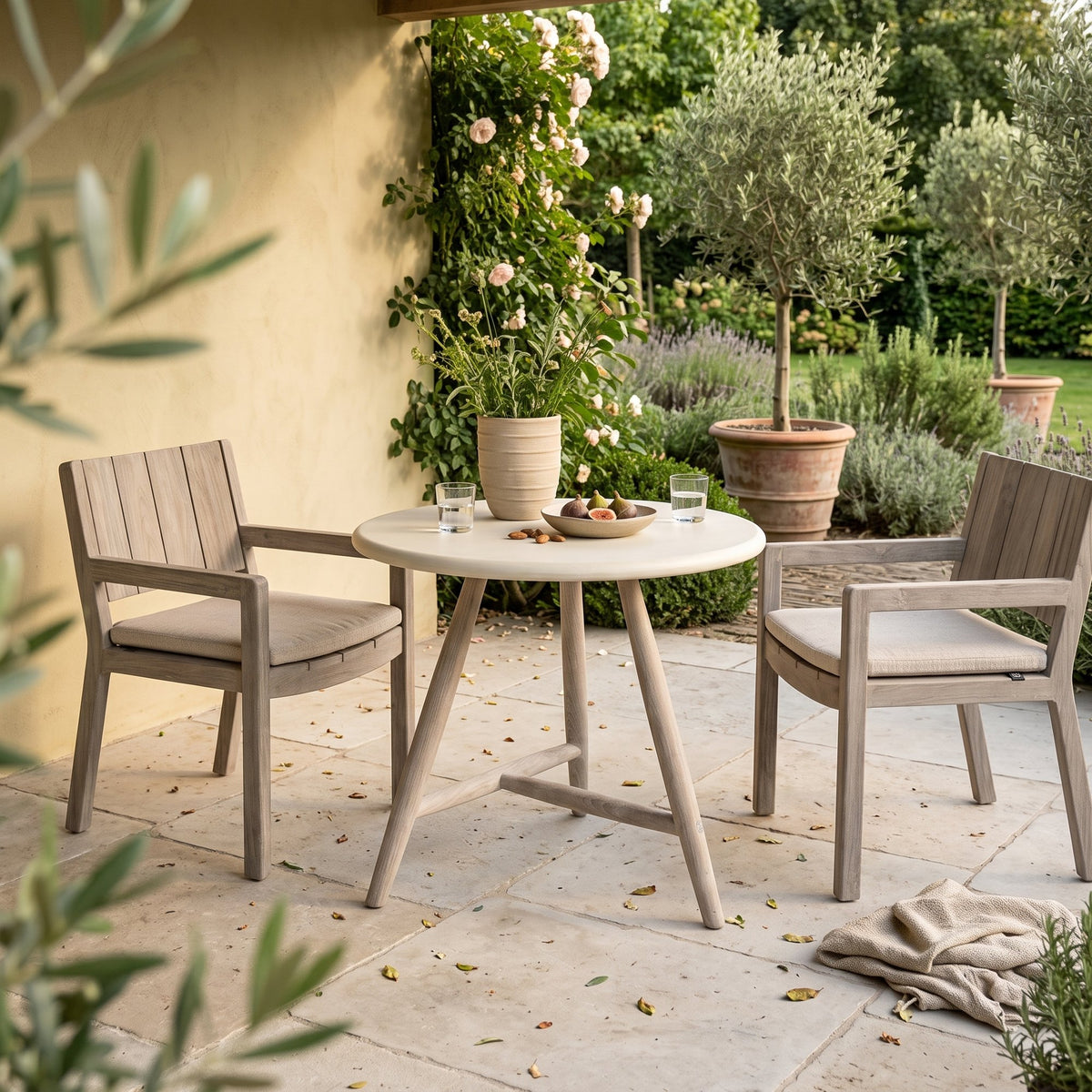 Bistrotisch Faye rund Beton Teak Natural Grey von Gommaire, Beton und Teak Natural Grey, Ø 75 × H 76 cm, Ambiente mit Armlehnenstühlen Mario und Vase Simon auf der Gartenterrasse