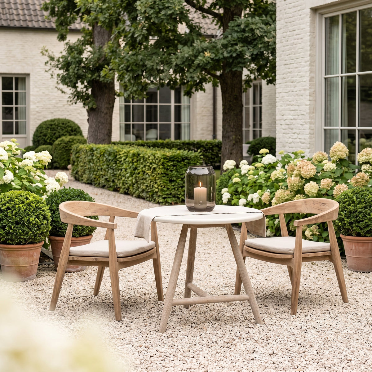 Bistrotisch Faye rund Beton Teak Natural Grey Low von Gommaire, Beton und Teak Natural Grey, Ø 75 × H 69 cm, Interiorbild mit Sesseln Faye und Windlicht Daniel im Kiesgarten