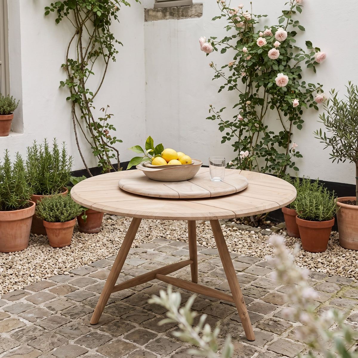Drehteller Lazy Faye Teak Natural Grey von Gommaire, Teak Natural Grey, Ø 70 × H 3,5 cm, Ambiente mit Esstisch Faye rund und Schale Ali im Innenhof
