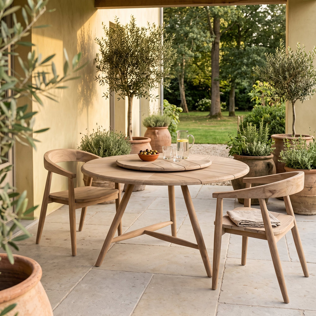 Drehteller Lazy Faye Teak Natural Grey von Gommaire, Teak Natural Grey, Ø 70 × H 3,5 cm, Ambiente mit Esstisch Faye rund und Armlehnstühlen Faye auf der Gartenterrasse