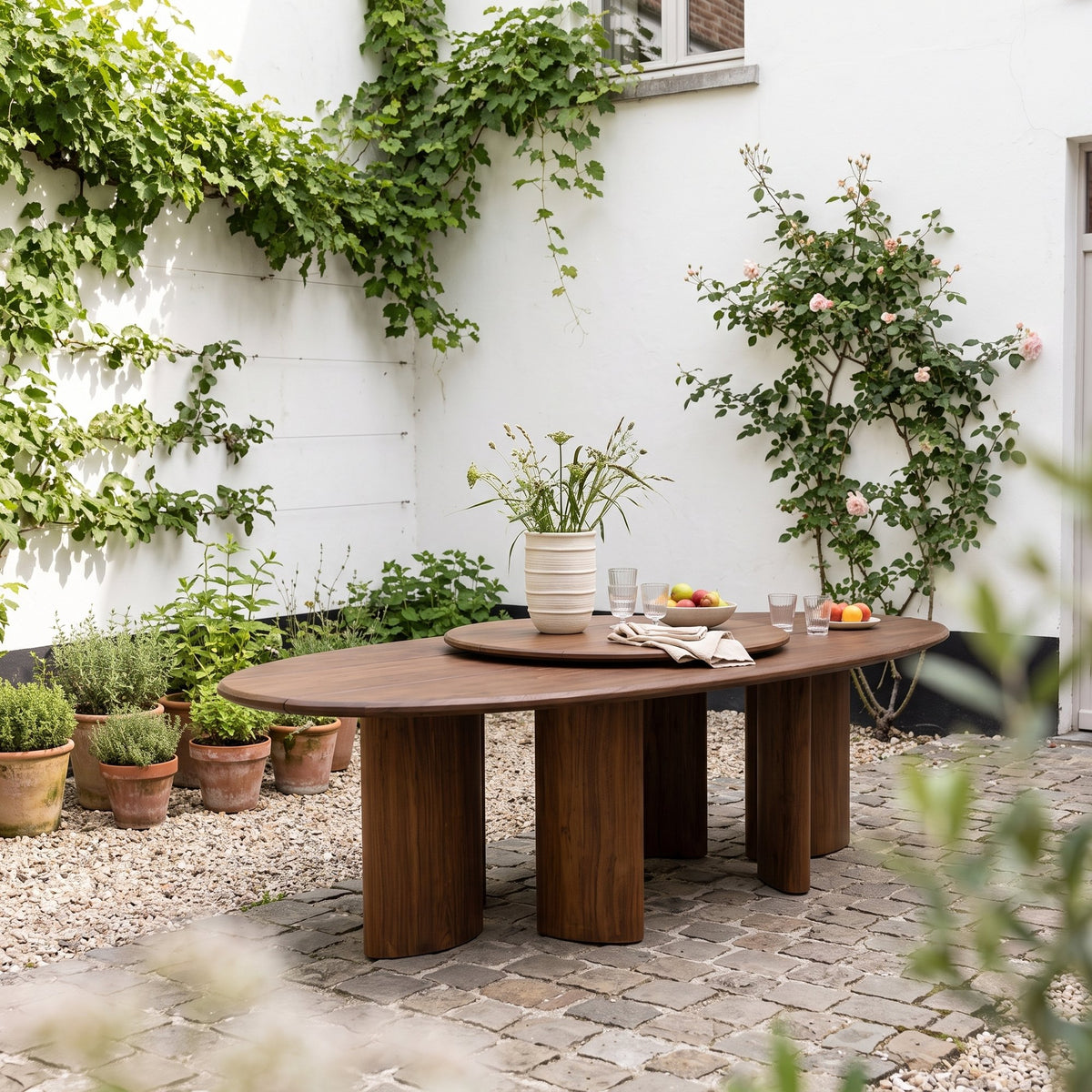 Drehteller Lazy Imen Teak Emas Brown von Gommaire, Teak Emas Brown, Ø 100 × H 3,5 cm, auf dem Outdoor Tisch Imen Oval mit Vase Simon im Innenhof