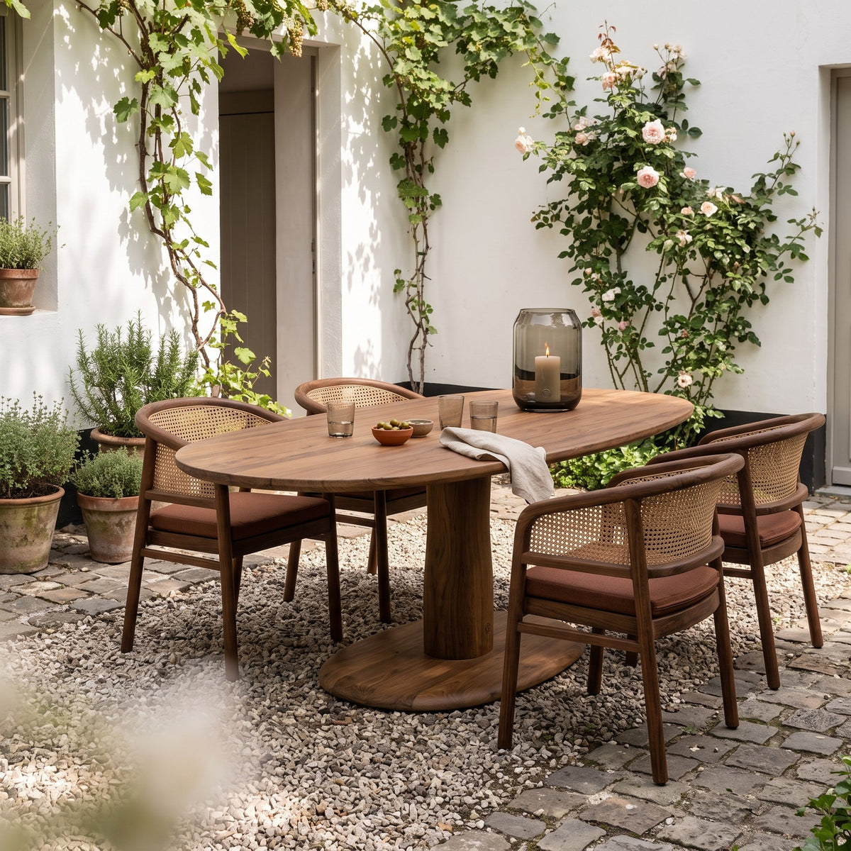 Esstisch Dita Rectoval Teak Emas Brown von Gommaire, Teak Emas Brown, 180 × 112,5 × H 76 cm, mit Armlehnenstühlen Imen und Windlicht Daniel im Innenhof