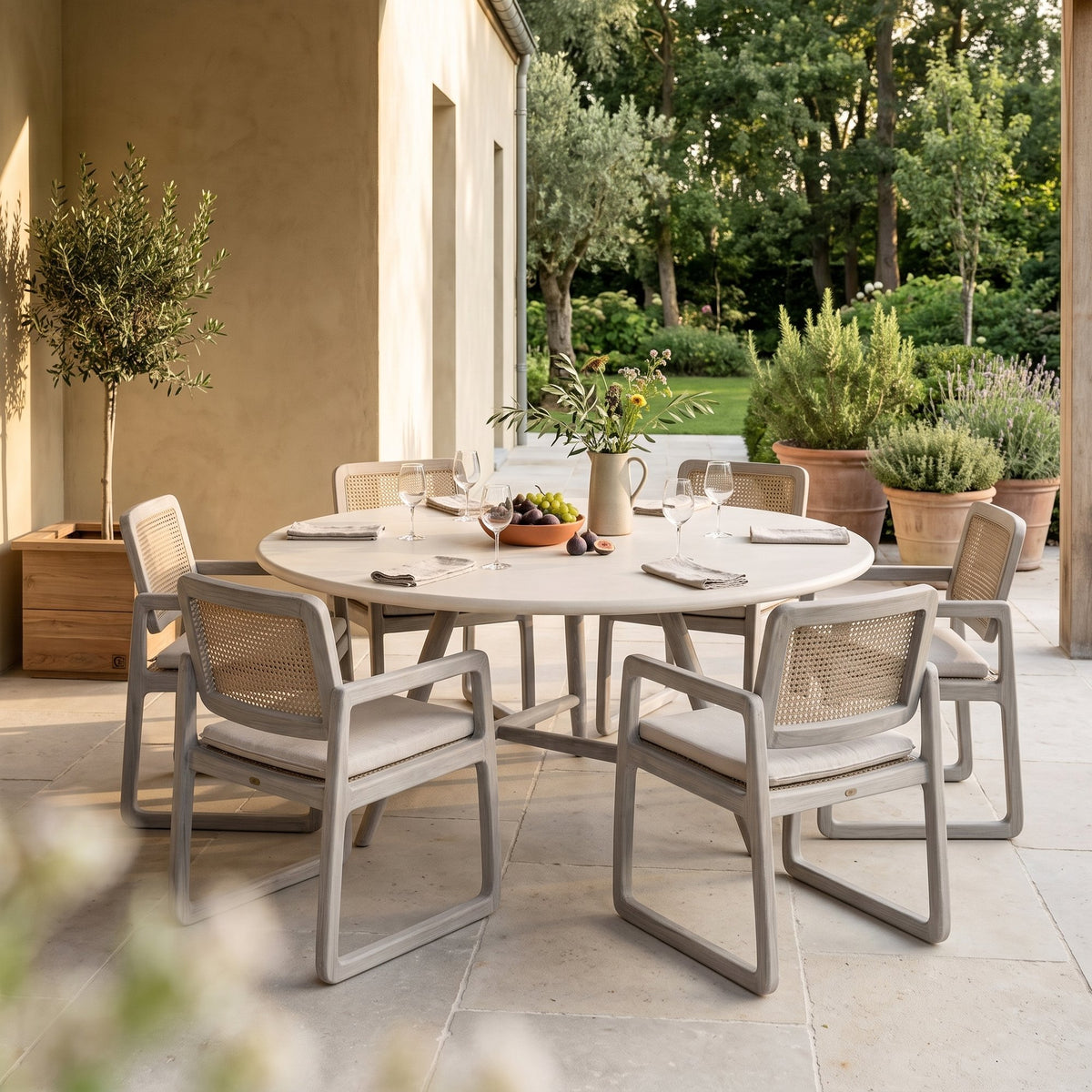 Esstisch Faye rund Beton Teak Natural Grey XL Low von Gommaire, Beton und Teak Natural Grey, Ø 170 × H 69 cm, Ambiente mit Loungesesseln Sally Open Weave und Pflanzkübel Ferdy auf der Gartenterrasse