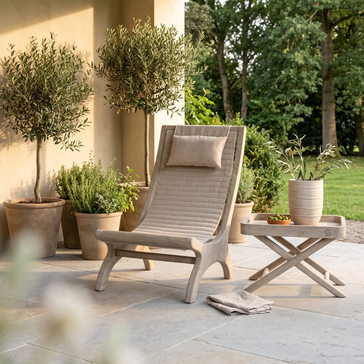 Loungesessel Beacher Sachin Teak Natural Grey Brushed Oak von Gommaire, Teak Natural Grey, Bespannung Sunbrella Brushed Oak, B 60 × T 97 × H 97,5 cm, mit Tabletttisch James Small und Vase Simon auf der Gartenterrasse