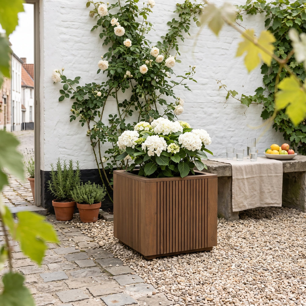 Pflanzkübel Nora Teak Emas Brown Large von Gommaire, Teak Emas Brown, 60 × 60 × H 60 cm, mit Hortensie an der Hauswand im Innenhof