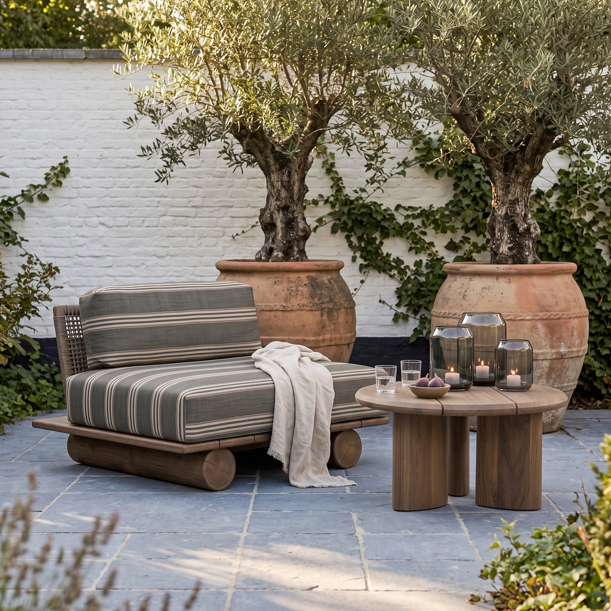 Sessel Edge Teak Emas Brown von Gommaire mit Couchtisch Imen rund Teak Emas Brown Small und Windlicht Daniel Rauchglas auf der Gartenterrasse