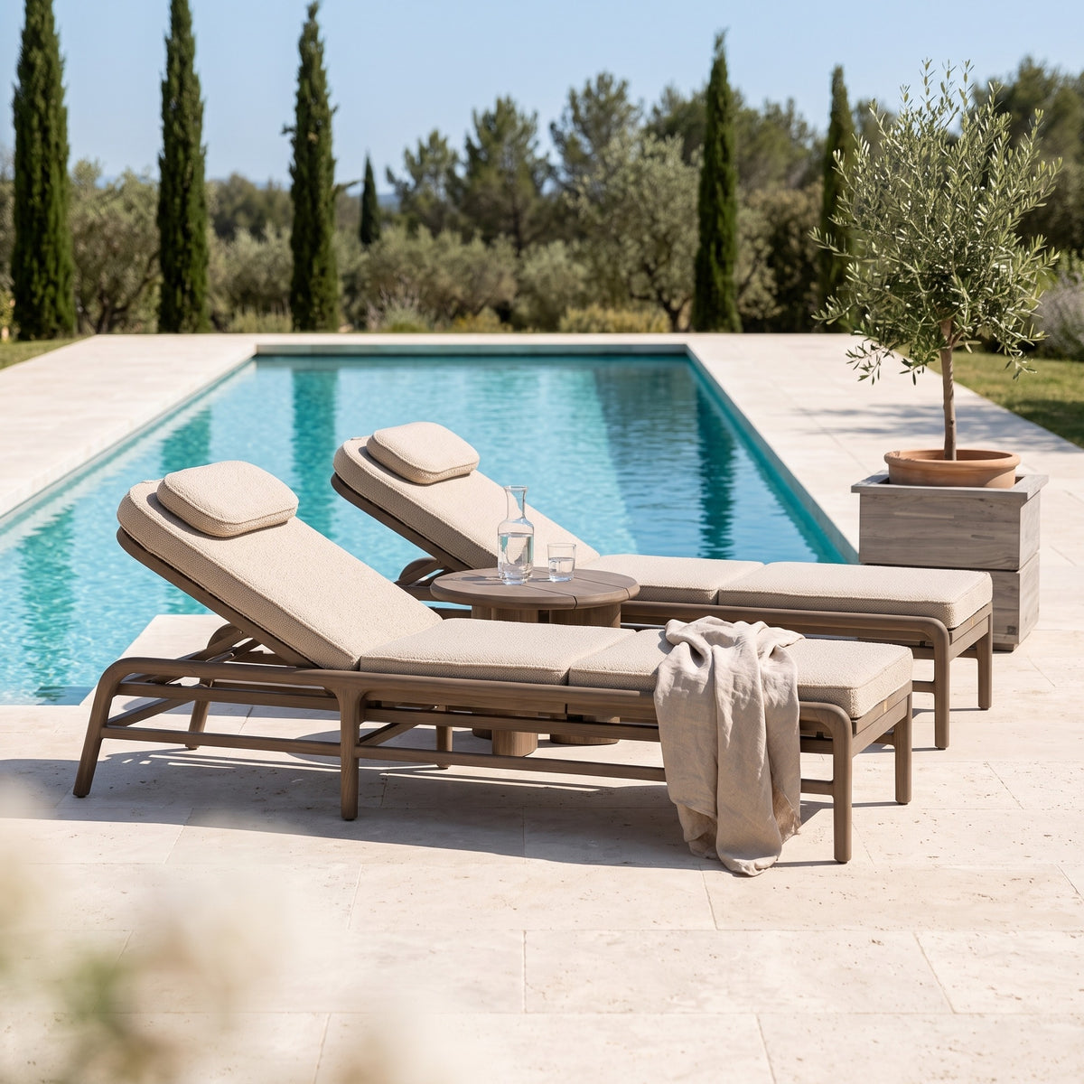 Sonnenliege Imen Teak Emas Brown PE Rattan von Gommaire paarweise mit Couchtisch Imen rund Teak Emas Brown Small und Pflanzkübel Ferdy am Pool