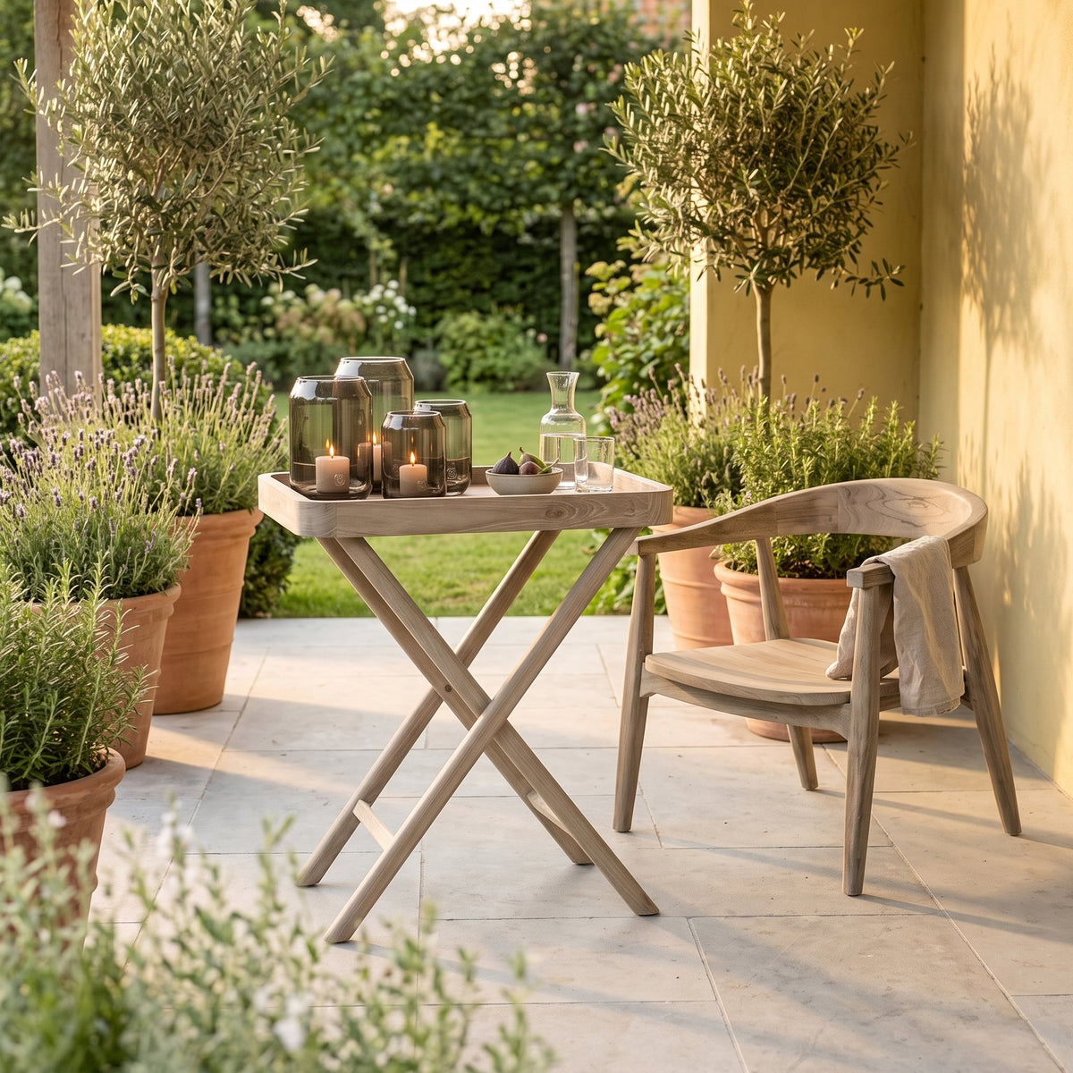 Tabletttisch James Teak Natural Grey Large von Gommaire, Teak Natural Grey, 65 × 45 × H 80 cm, neben einem Sessel Faye Easy Chair mit Windlicht Daniel auf der Gartenterrasse